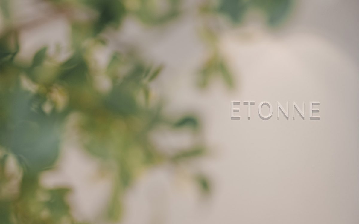 초록 잎 사이로 흐릿하게 보이는 벽면의 ETONNE 로고