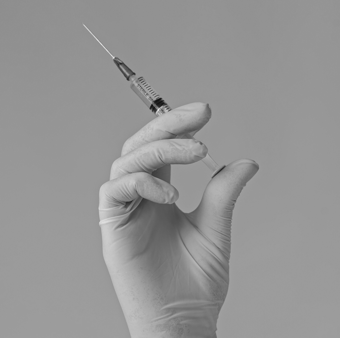 Black-and-white photo of a gloved hand holding a syringe